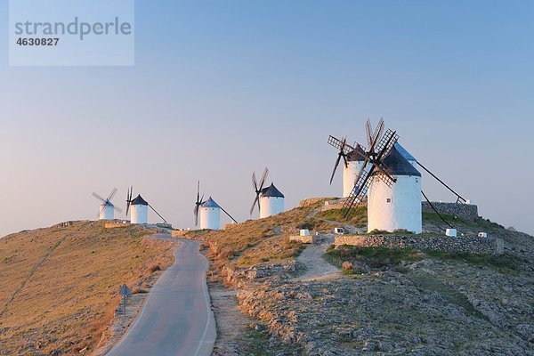 Spanien  Provinz Toledo  Kastilien-La Mancha  Reihe von Windmühlen mit Landstraße bei Sonnenaufgang