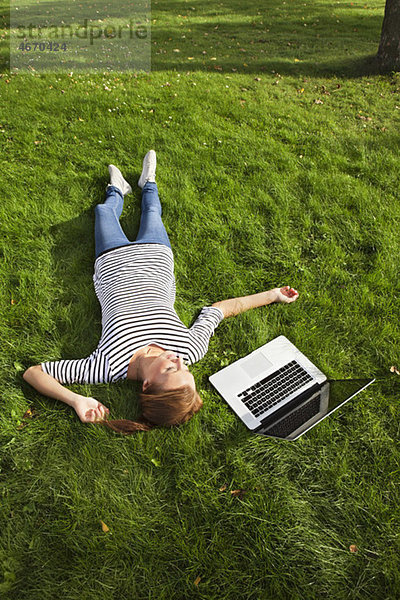 Frau im Gras neben dem Computer liegend