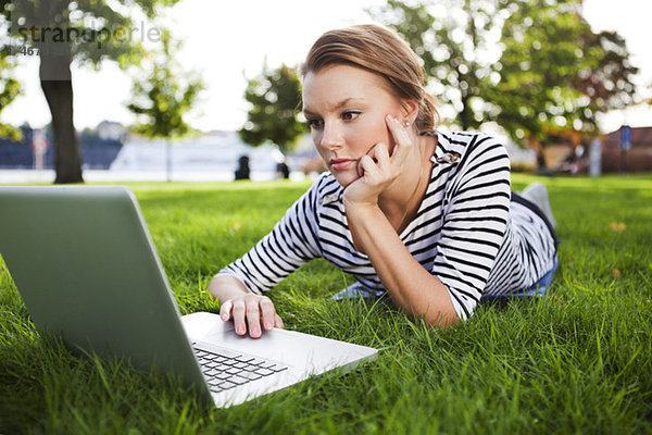 Frau im Gras liegend mit Computer