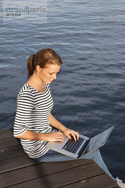 Frau am Steg sitzend mit Computer im Schoß