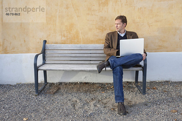 Mann sitzt auf der Bank mit Computer auf dem Schoß