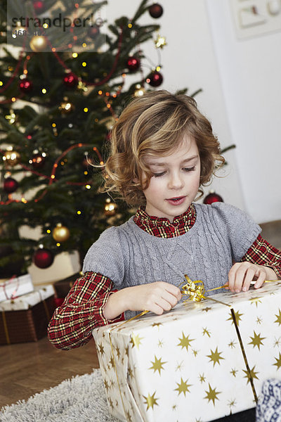 Mädchen mit großem Geschenk vor dem Baum