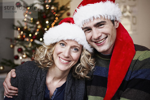 Paar mit Weihnachtsmützen vor dem Baum
