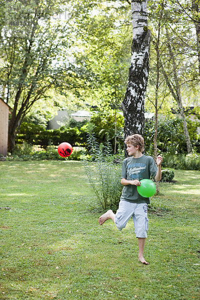 Junge spielt mit zwei Bällen im Garten