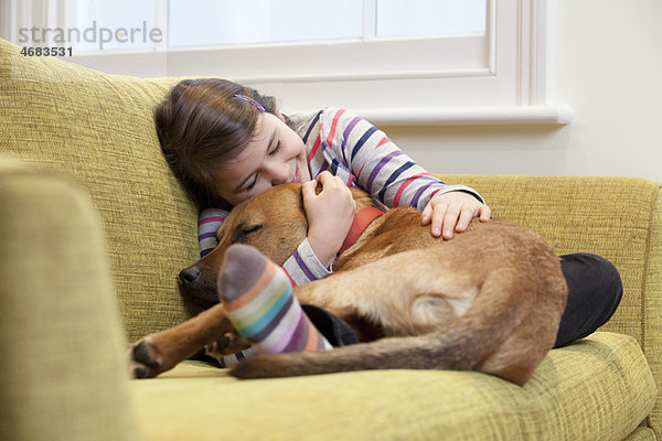 Junges Mädchen kuschelt ihren Hund auf dem Sofa