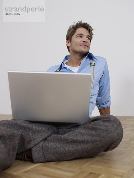 Junger Mann mit Laptop in leerer Wohnung