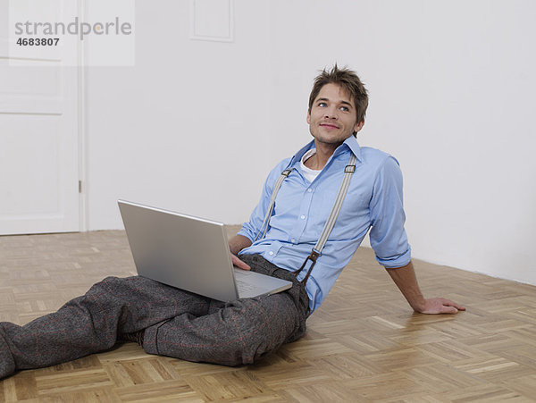 Junger Mann mit Laptop in leerer Wohnung
