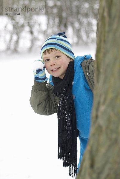 Junge versteckt sich hinter Baum mit Schneeball