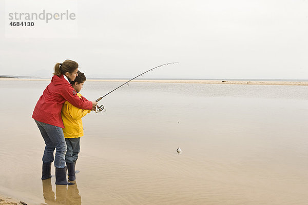 Mutter bringt dem Sohn das Fischen am Strand bei.