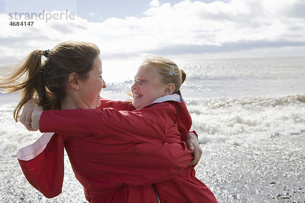 Mutter und Tochter umarmen sich am Strand