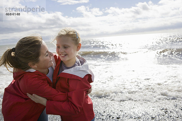 Mutter und Tochter umarmen sich am Strand