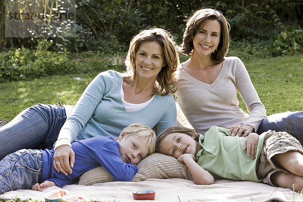 Zwei fröhliche Frauen mit zwei Kindern auf einer Decke im Freien