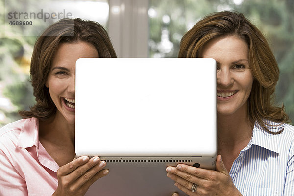 Zwei fröhliche Frauen halten Laptop