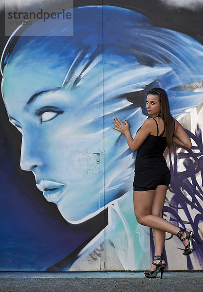Junge Frau mit Hotpants und hochhackigen Schuhen posiert vor Graffitiwand
