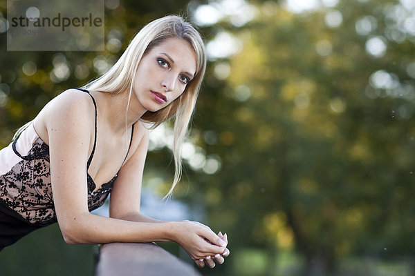 Portrait einer jungen Frau mit langen blonden Haaren an Brückengeländer