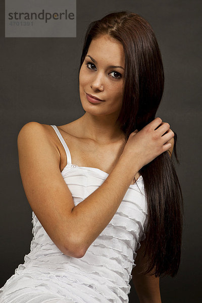 Junge Frau mit langen braunen Haaren und weißem Kleid posiert