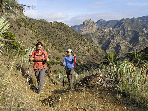 Mann und Frau mit Wanderstöcken wandern im Barranco de la Era Nueva  hinten Roque Cano  Vallehermoso  La Gomera  Kanaren  Spanien  Europa