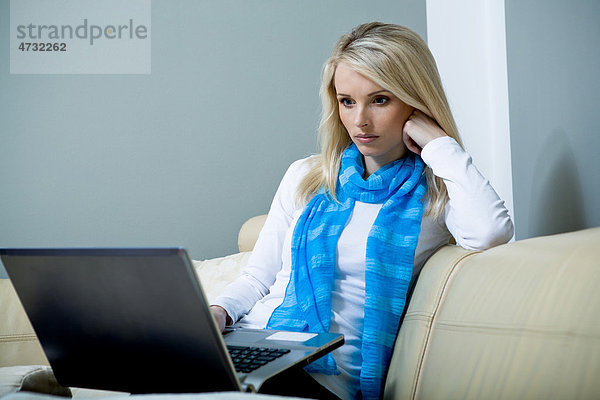 Eine junge Frau mit einem Laptop auf dem Sofa