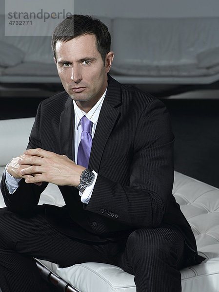 Businessmann im Anzug sitzend auf weißem Sofa