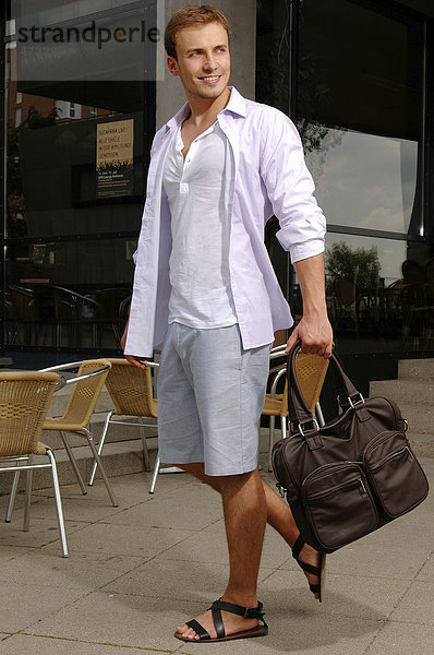 Junger Mann in kurzer Hose und Sandalen mit Tasche beim Shoppen