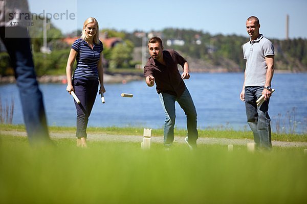 Vier Erwachsene spielen Kubb auf Gras am Meer
