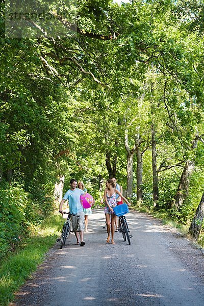 Vier junge Menschen mit Fahrrädern zu Fuß auf ländliche Straße