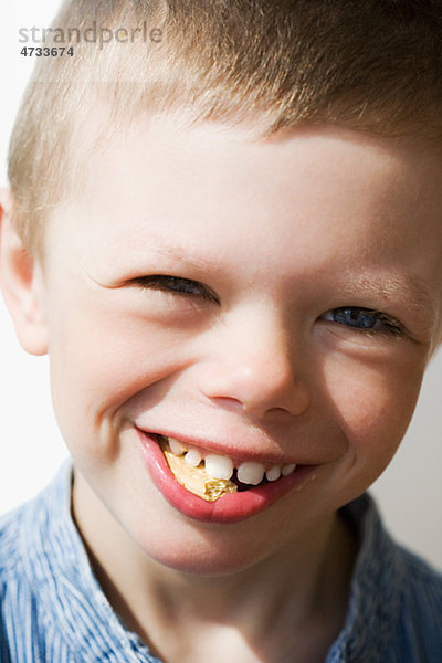 Junge lächelt mit Biscuit im Mund