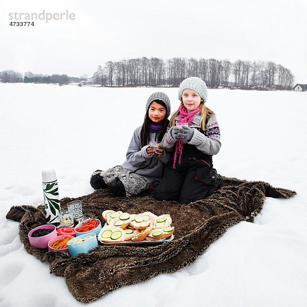 Portrait von zwei Mädchen mit Picknick im Schnee