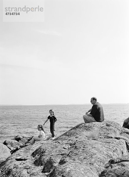 Mädchen und älterer Mann auf Felsen mit Meer im Hintergrund