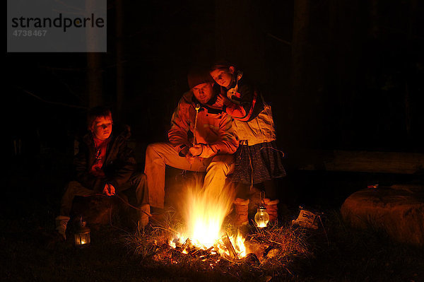 Vater sitzt mit seinen Kindern um ein Lagerfeuer