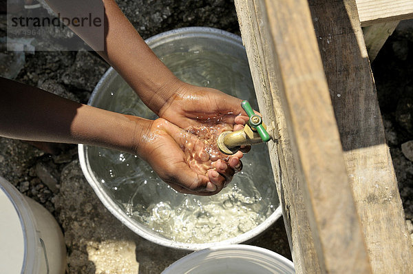 Kind füllt die geöffneten Hände mit sauberem Wasser  Trinkwasserversorgung durch eine Hilfsorganisation in einem Armenviertel  Petit Goave  Haiti  Karibik  Zentralamerika