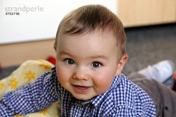 Kleiner Junge  6 Monate  liegt auf dem Bauch auf einer Spieldecke in seinem Kinderzimmer  lächelt  Deutschland  Europa