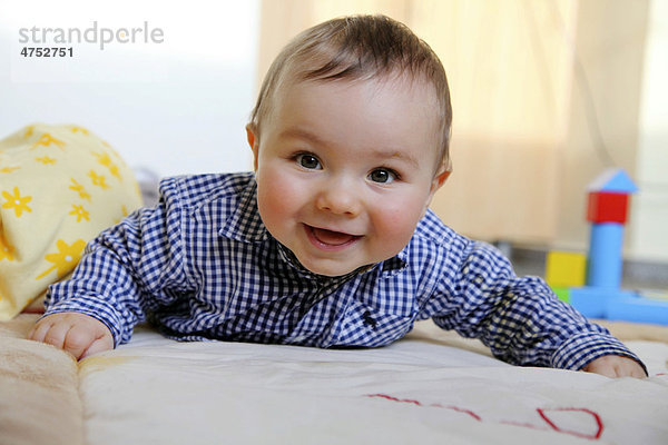 Kleiner Junge  6 Monate  liegt auf dem Bauch auf einer Spieldecke in seinem Kinderzimmer  lächelt  Deutschland  Europa