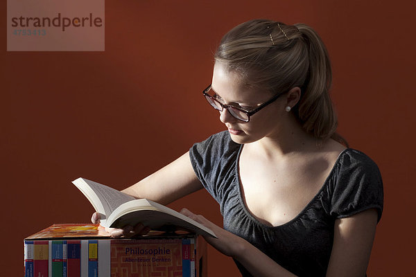 Junge Frau sitzt neben einem Hocker und liest ein Buch