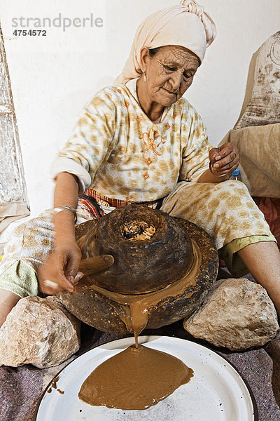 Für die traditionelle Herstellung von Arganöl mahlt eine Frau bei Essaouira geröstete Argan-Mandeln zwischen zwei Mahlsteinen  Marokko  Afrika