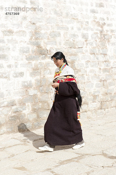 Tibetischer Buddhismus  junge gläubige Tibeterin läuft an einer Mauer entlang  Ganden-Kloster  Himalaja  Zentraltibet  Ü-Tsang  Autonomes Gebiet Tibet  Volksrepublik China  Asien