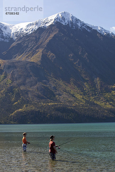 Zwei Jungen stehen im seichten Wasser und angeln am See Kathleen Lake  dahinter der Berg King's Throne  St. Elias Mountains  Eliaskette  Kluane-Nationalpark  Yukon Territorium  Kanada
