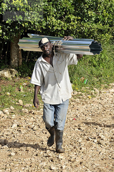 Mann trägt Wellblech für die Dachdeckung. Nach dem schweren Erdbeben im Januar 2010 bildet eine deutsche Hilfsorganisationen lokale Bauarbeiter im Bau erdbebensicherer Häuser aus  Dorf Coq Chante nahe Jacmel  Haiti  Karibik  Zentralamerika
