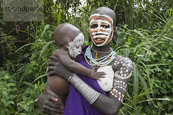 Surma Frau mit Gesichtsbemalung und Körperbemalung hält ihr Baby im Arm  Kibish  Omo-Tal  Äthiopien  Afrika