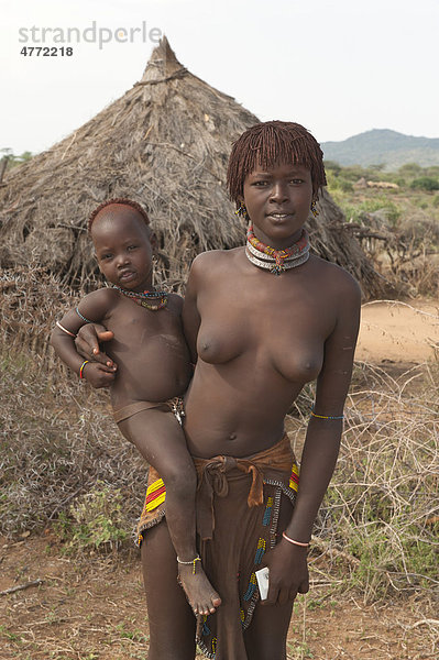 Junge Hamar Frau mit traditioneller Haarfrisur aus rotem Lehm hält ein Baby im Arm  Omo-Tal  Süd Äthiopien  Afrika