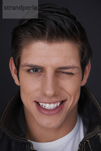 Junger Mann mit strahlend weißen Zähnen zwinkert  Porträt