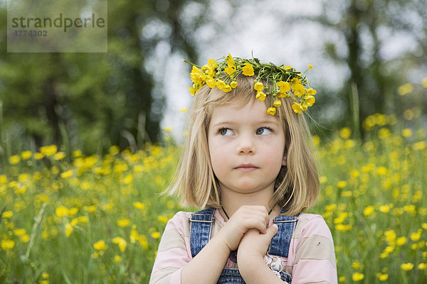 Mädchen mit einem Blumenkranz auf dem Kopf  verschränkten Händen und einem fragenden Blick  Porträt