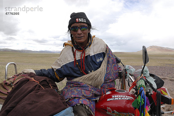 Tibetischer Pilger sitzt mit Sonnenbrille auf geschmücktem und bepacktem Motorrad auf dem Weg zum Berg Kailash  Hochebene Changtang bei den Lungkarbergen  Westtibet  Provinz Ngari  Tibet  China  Asien