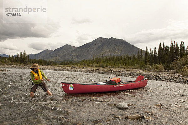 Junge Frau beim Treideln  watet durch flaches Wasser und zieht ein Kanu hinter sich her  Wind River  Mackenzie Mountains  Yukon Territory  Kanada