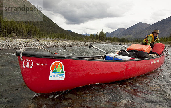 Junge Frau watet durch flaches Wasser und schiebt ein Kanu vor sich her  Wind River  Mackenzie Mountains  Yukon Territory  Kanada