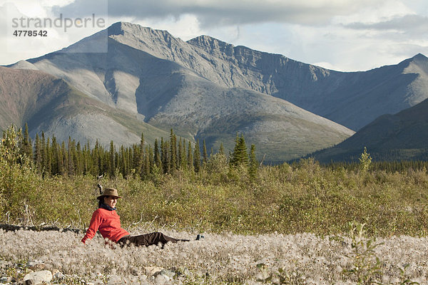 Junge Frau sitzt entspannt im Gras  Wollgras  und genießt die Abendsonne  Northern Mackenzie Mountains  Wind River  Yukon Territory  Kanada