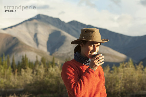 Junge Frau genießt eine Tasse Tee  Wind River  hinten nördliche Mackenzie Mountains Gebirgskette  Yukon Territorium  Kanada