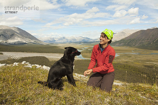 Junge Frau spielt mit ihrem Hund  Alaskan Husky  Schlittenhund  Aussicht  Wind River Tal und Mackenzie Mountains hinter  Yukon Territory  Kanada