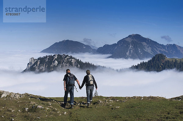 Wanderer Hand in Hand am Berg  schauen über Hochnebel zu Berggipfeln der Chiemgauer Alpen  Oberbayern  Bayern  Deutschland  Europa