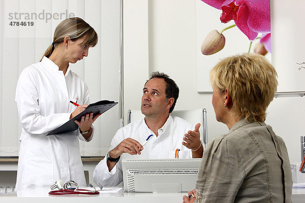 Arztpraxis  Arzt im Gespräch mit einer Patientin  bespricht mit ihr und einer Praxishilfe die anstehenden Untersuchungen